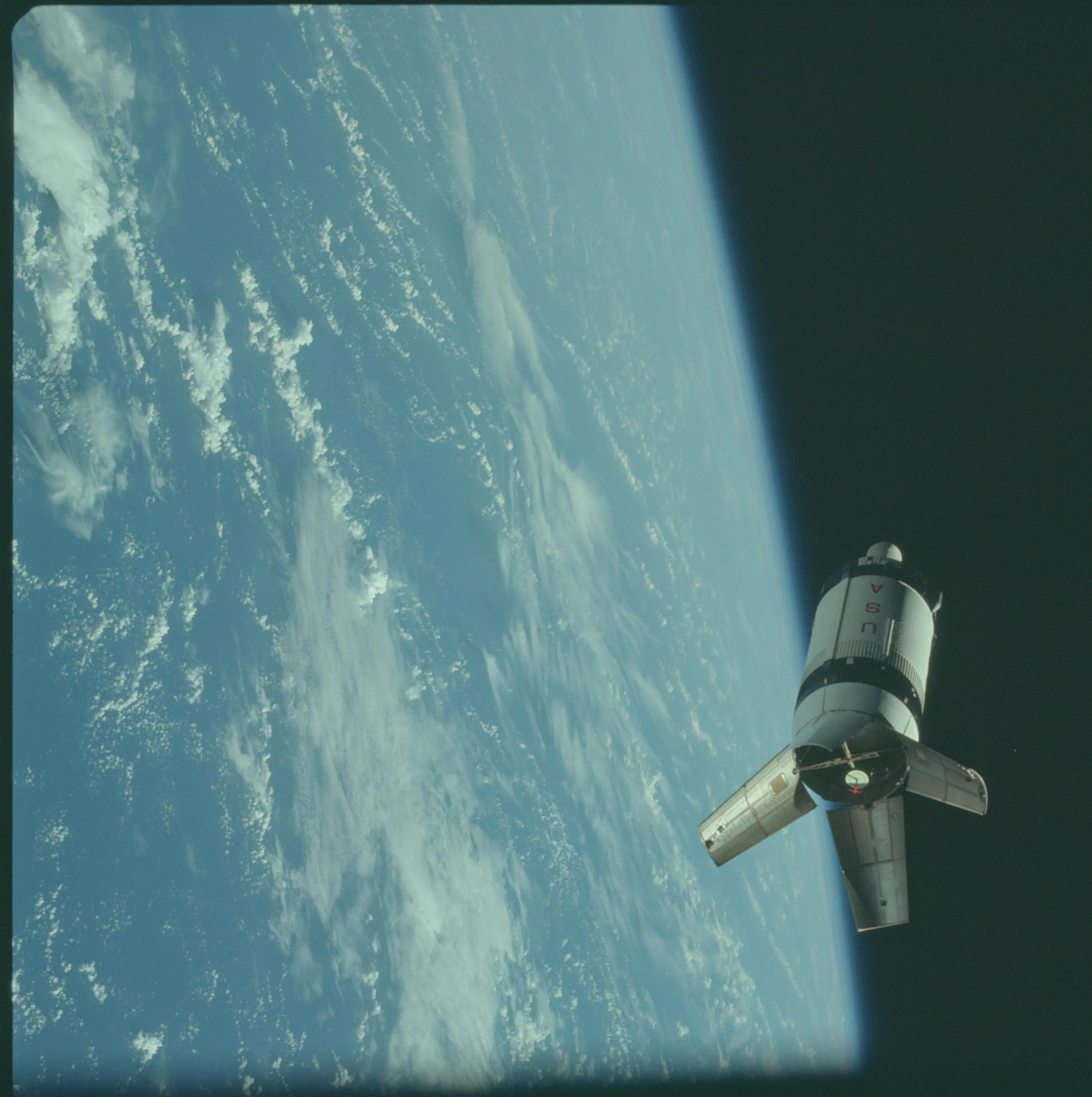 A spacecraft orbits above Earth, with the planet's surface partially covered by clouds against the dark background of space, reminiscent of Bill Anders' iconic Earth photographs.